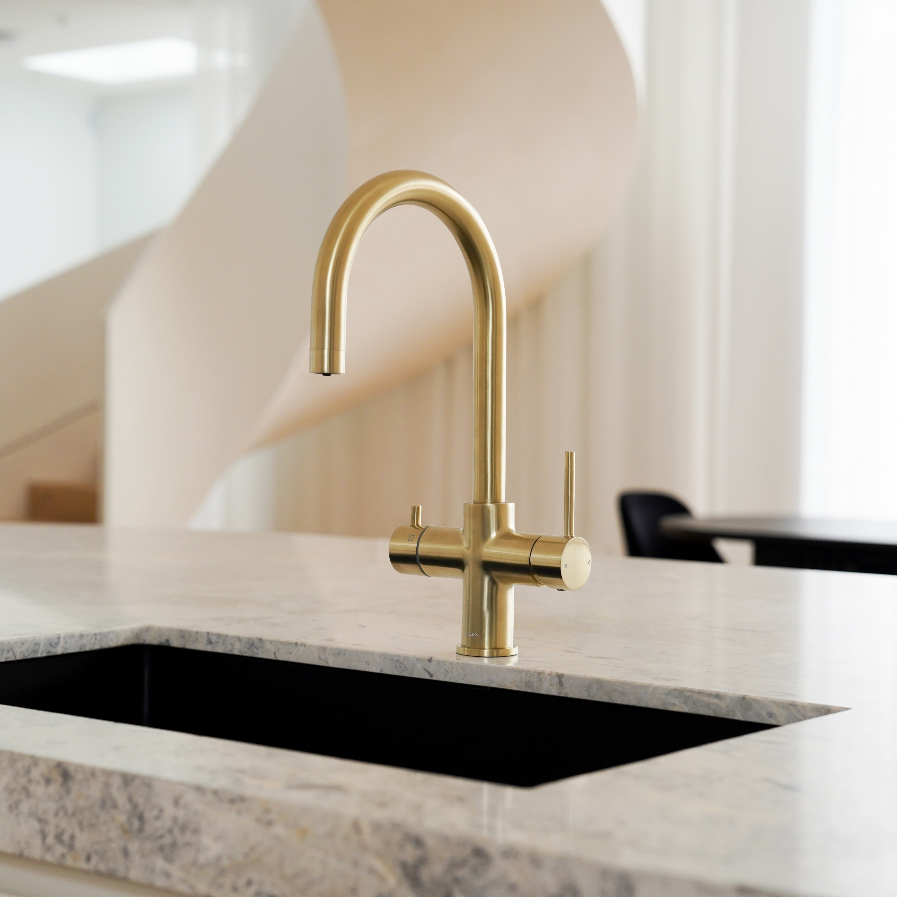 Brushed gold Alia Global 4-in-1 instant hot filtered water tap installed in a luxury kitchen setting, combining elegant style with advanced water dispensing capabilities.
